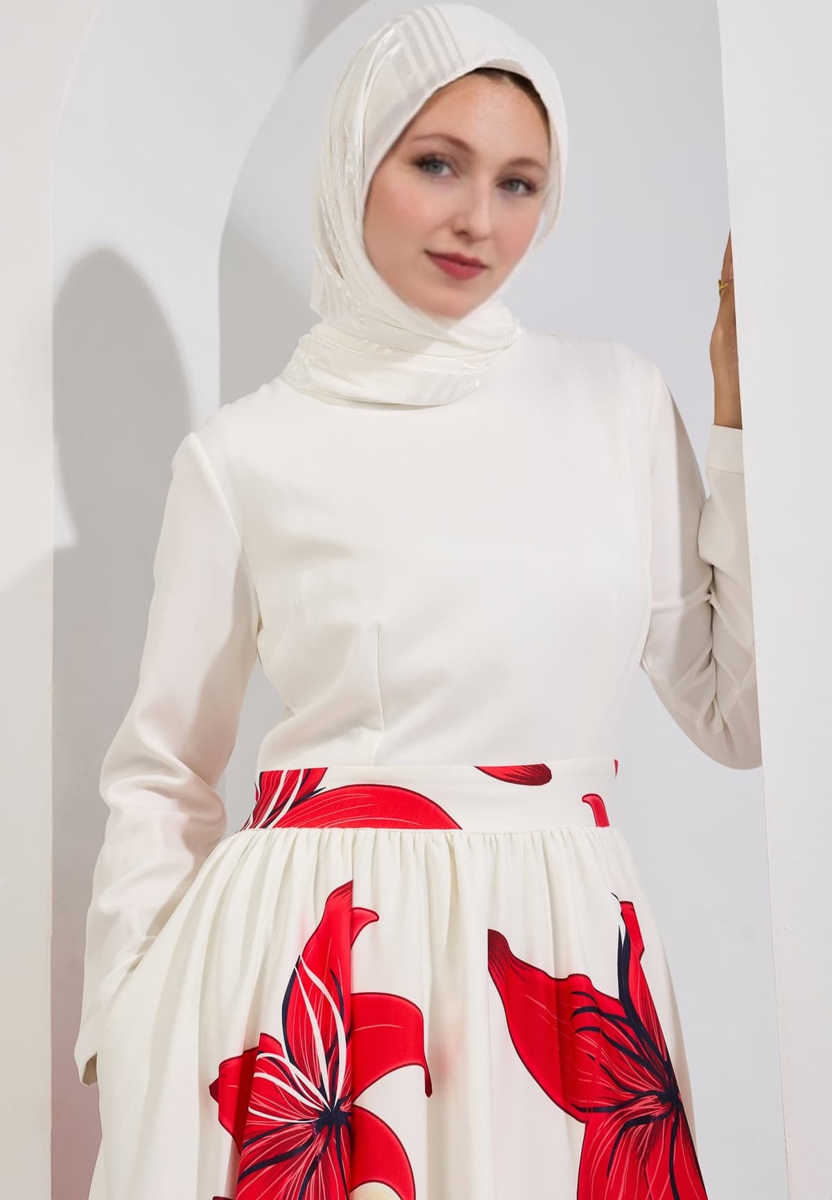 A seated model in the Radiant Blossom Crepe Maxi Dress, showing the intricate red floral design