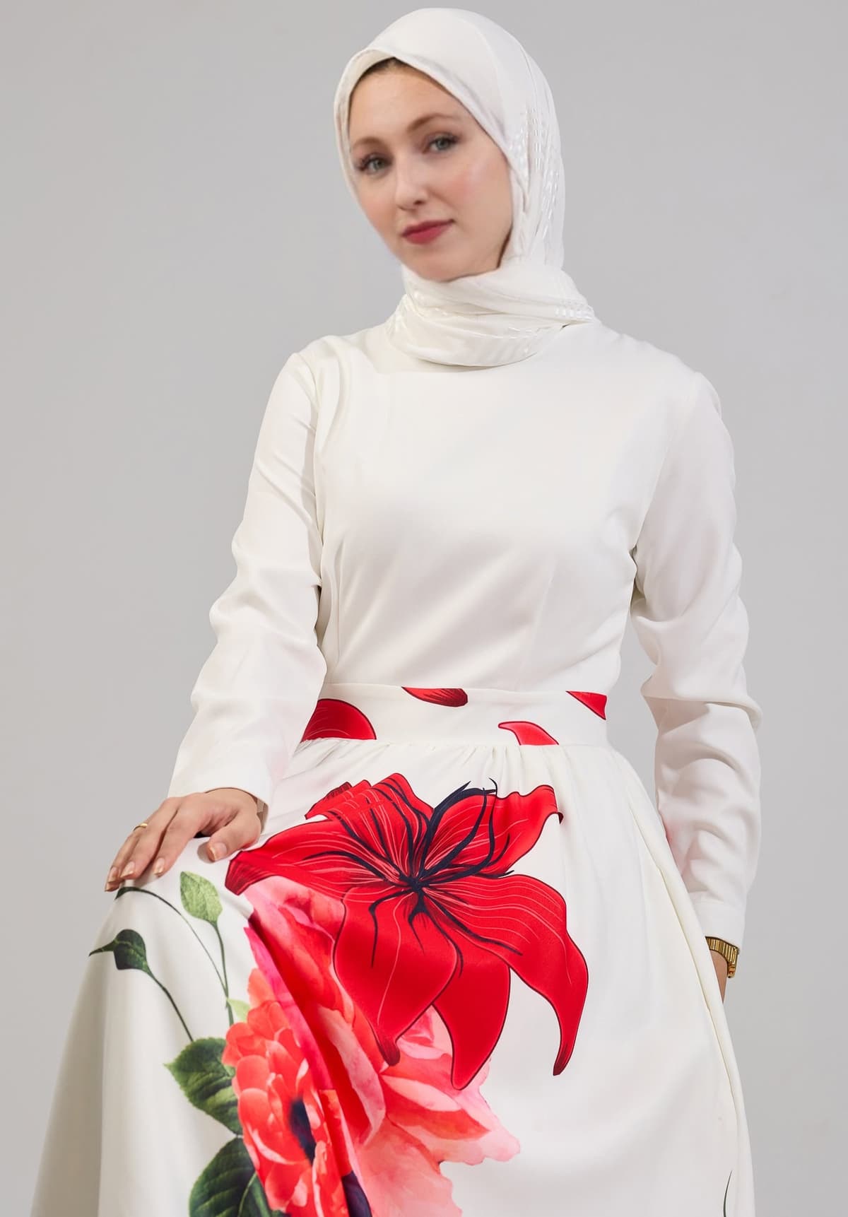 A seated model in the Radiant Blossom Crepe Maxi Dress, showing the intricate red floral design